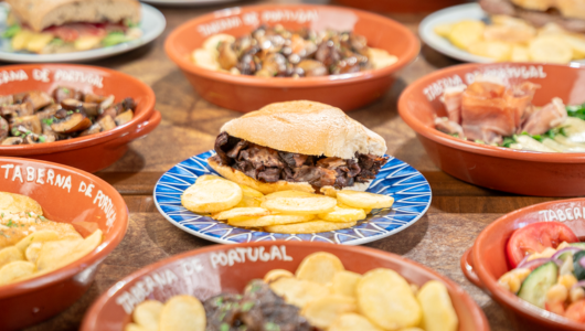 Portuguese dishes with a sandwich and chips on a decorative plate surrounded by small bowls.