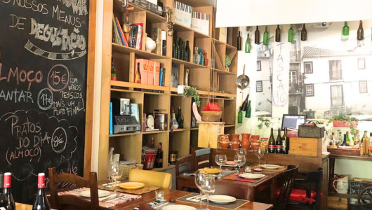 Cozy restaurant interior with wooden shelves, chalkboard menu, and tables set with wine glasses.