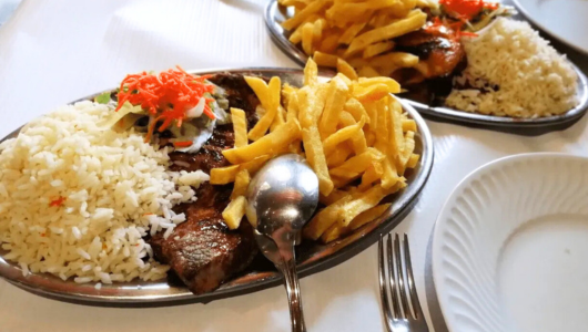 Platters with steak, rice, fries, and garnish on a table with a fork and plate.