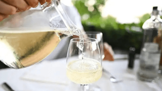 White wine being poured into a clear glass on a table.
