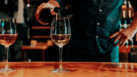 Person pouring wine into a glass on a wooden table.