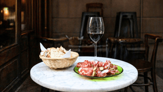 Marble table with wine, charcuterie, and bread outside a café.