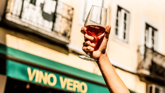 Hand holding a glass of wine in front of a building with 'Vino Vero' sign.