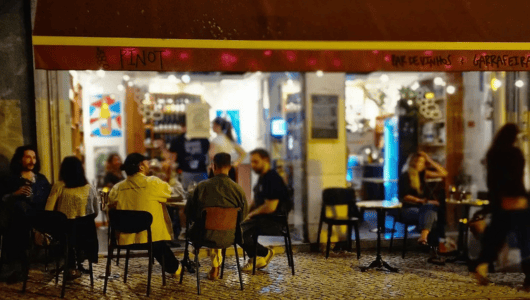 People sitting at an outdoor cafe with a red awning in the evening.