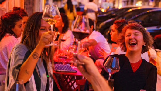 Group of people laughing and toasting with wine glasses at an outdoor gathering.