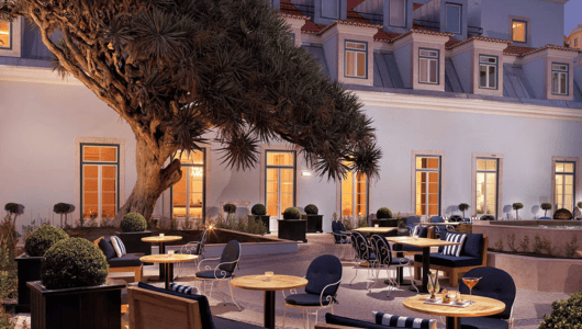 Outdoor patio with chairs, tables, and a large tree against a building's lit windows.