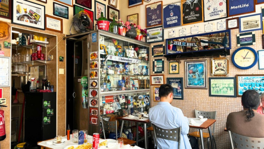 Cafe interior with framed memorabilia on walls, tables, and two seated people.