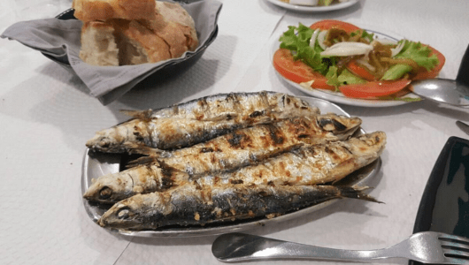 Grilled fish on a plate with bread and salad on a table.