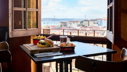 Burger and fries on table by window overlooking city and bridge.