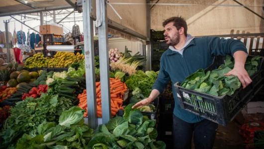 a man standing in front of a store filled with lots of fresh produce