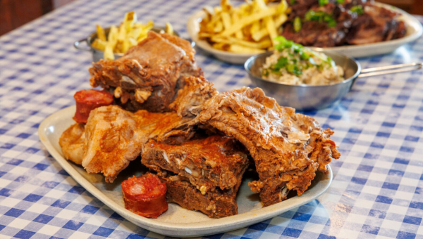 00.Moita travel guide for food lovers_feat photo Plate of assorted meats with a side of fries and a bowl of creamy dish on a checkered tablecloth.
