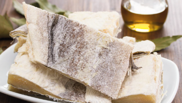 00.What Portuguese people usually have in their pantry_feat photo Dried salted cod fish pieces on a white plate with olive oil in the background.