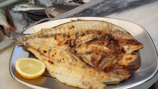Grilled fish served on a plate with lemon wedge.