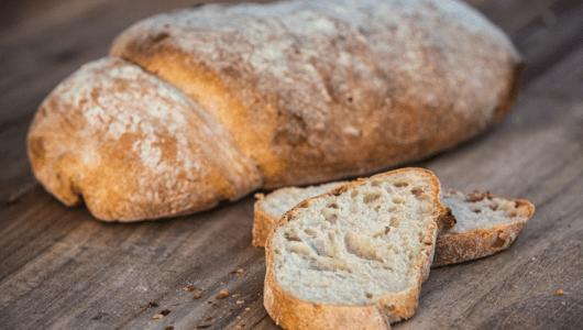 Loaf of rustic bread with two slices on wooden surface.