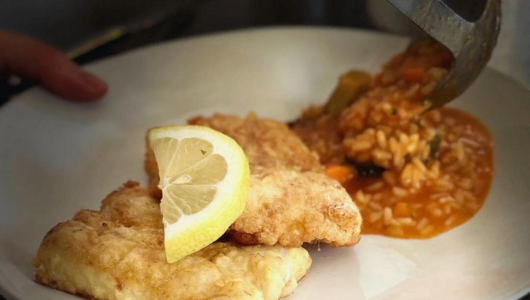 Plate with two fried fish fillets, lemon wedge, and rice being served from a ladle.