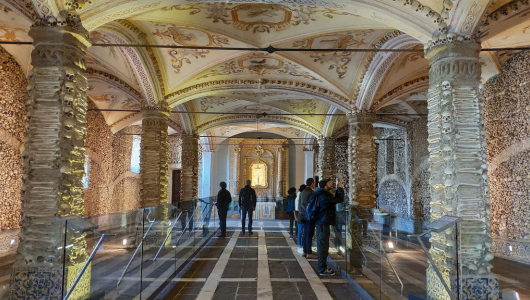 People in a dimly lit ornate room with stone pillars and arched ceilings.