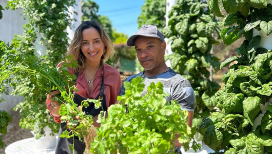 Two people holding fresh greens in a vertical garden with leafy plants.