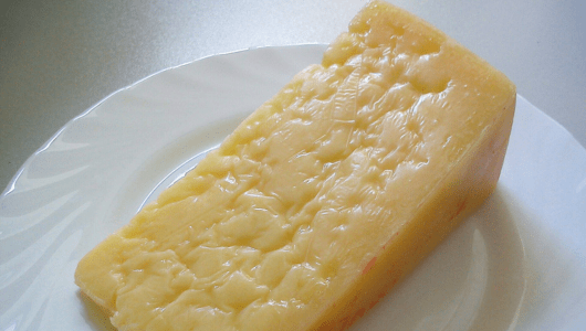 A block of yellow cheese on a white plate.