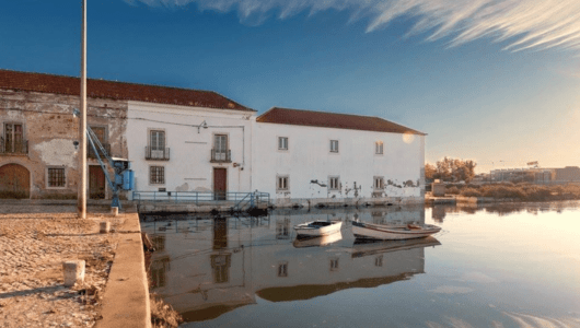 Two small boats on calm water near an old waterfront building under a clear sky.