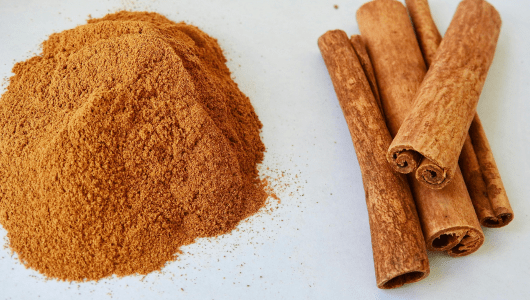 A pile of ground cinnamon beside whole cinnamon sticks on a white background.