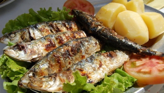 Plate with grilled fish on lettuce, sliced tomato, and boiled potatoes.
