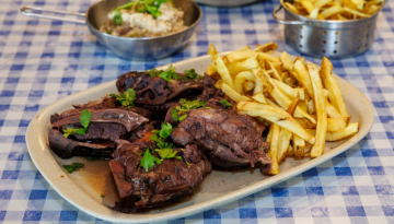 Plate of cooked meat and fries on a blue checkered tablecloth.