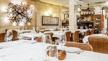 Elegant restaurant with white tablecloths, wicker chairs, and decorative wall art.