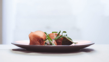 Side view of a gourmet dish on a plate with arugula and thin meat slices.