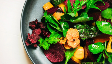 Close-up of colorful salad with greens, beets, and orange slices in a black bowl.