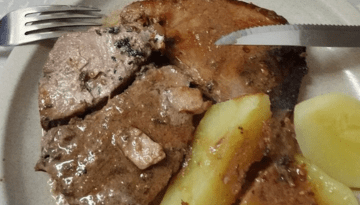 Plate with slices of cooked meat and boiled potatoes with a fork and knife.