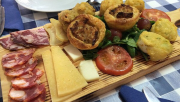 Wooden board with assorted cheeses, cured meats, pastries, and vegetables.