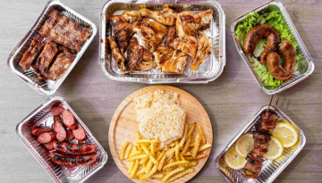 Assorted grilled meats in trays with rice and fries on a wooden board.