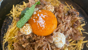 Gourmet dish with shredded meat, whole egg yolk, garnished with mint and cheese balls in a dark bowl.