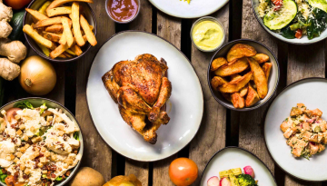 Roast chicken surrounded by various side dishes and sauces on a wooden table.