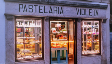 Front view of a pastry shop with illuminated displays filled with pastries.