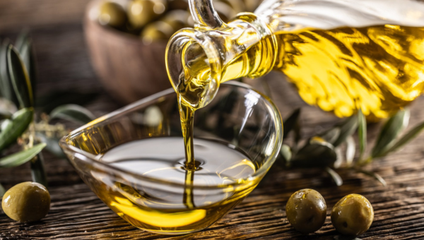 00.The Ultimate guide to olive oil in Portugal_feat photo Olive oil being poured into a glass bowl with olives in the background on a wooden table.