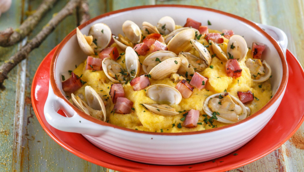00.The best corn dishes in Portugal_feat photo Bowl of polenta with clams, diced bacon, and herbs on a red plate.