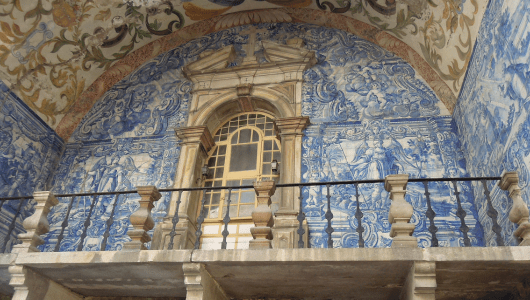 Ornate wall with blue tiles, arch, and balcony railing in historical building.