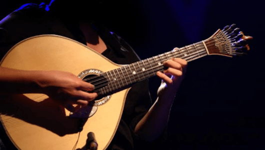 Person playing a Portuguese guitar on stage under dim lighting.