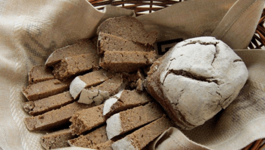 Basket of sliced brown bread with a whole loaf on cloth.