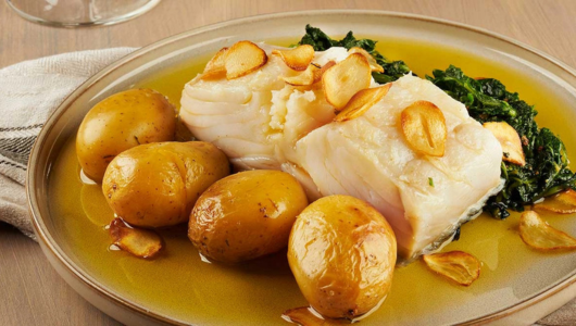 Plate with fish, sliced garlic, boiled potatoes, and greens.