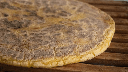 Close-up of a round, flat cornbread on a wooden surface.