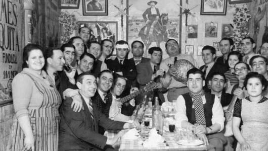 Group of people posing around a table in a vintage setting with a guitar and a leg of ham.