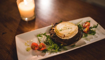 Grilled portobello mushroom topped with cheese, garnished with greens and cherry tomatoes on a rectangular plate.
