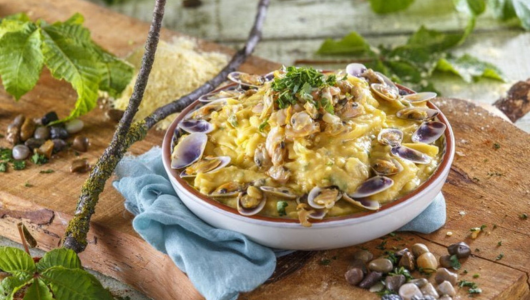 Creamy pasta with clams in a bowl on a wooden board, garnished with herbs.