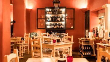Cozy restaurant with warm lighting, wine shelves, and neatly set tables and chairs.