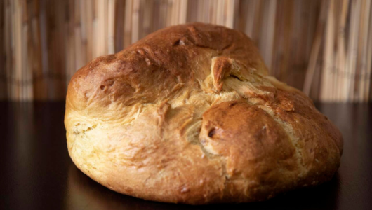 A round, rustic loaf of bread on a dark surface with a blurred wooden background.
