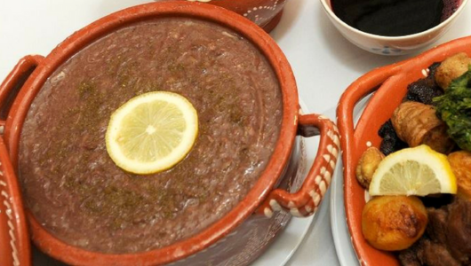 Clay pot of brown stew with a lemon slice, served with roasted vegetables on the side.