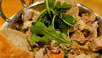 Dish with cooked meat, arugula, sesame seeds, and bread slices in a metal bowl.