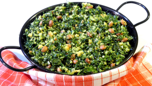Dish of cooked greens and beans in a black pan on a red checkered cloth.